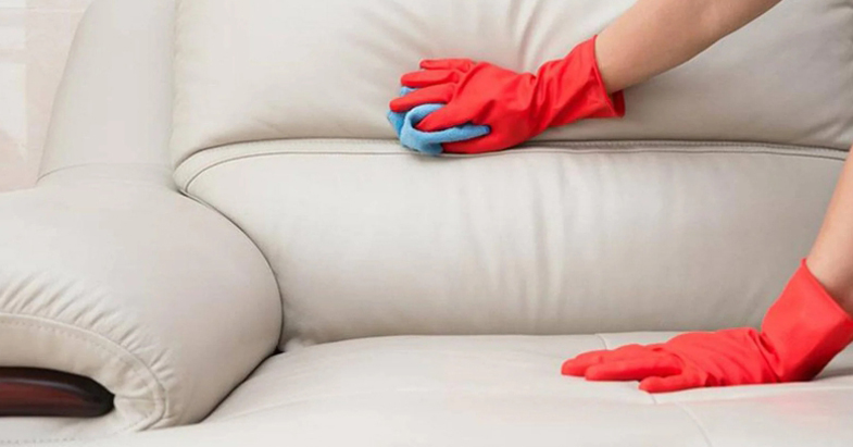 Person wearing red rubber gloves cleaning a white leather sofa with a blue cloth – leather lounge cleaning service