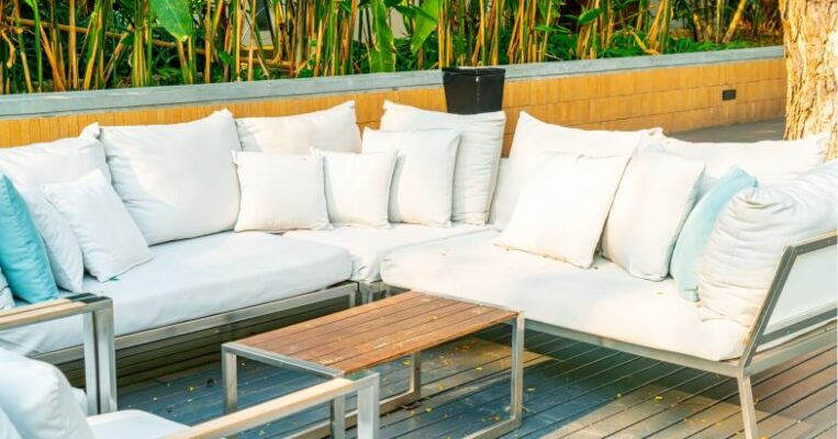 Outdoor modular lounge set with white cushions on a wooden deck surrounded by greenery